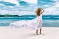 Happy beautiful young girl in fluttering in the wind of white cloth on a tropical beach. Blue sea in the background. Summer Royalty Free Stock Photo
