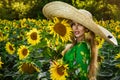 A happy, beautiful young girl in a straw big hat is standing in a large field of sunflowers. Beautiful woman posing in a field of Royalty Free Stock Photo