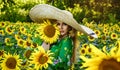A happy, beautiful young girl in a straw big hat is standing in a large field of sunflowers. Beautiful woman posing in a field of Royalty Free Stock Photo