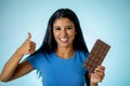 Happy beautiful young latin woman holding a big bar of chocolate with crazy excited face expression in sugar addiction and Royalty Free Stock Photo