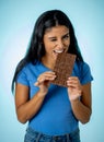 Happy beautiful young latin woman holding a big bar of chocolate with crazy excited face expression in sugar addiction and Royalty Free Stock Photo