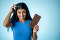 Happy beautiful young latin woman holding a big bar of chocolate with crazy excited face expression in sugar addiction and Royalty Free Stock Photo