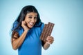 Happy beautiful young latin woman holding a big bar of chocolate with crazy excited face expression in sugar addiction and Royalty Free Stock Photo