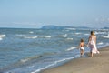 Happy beautiful young mom and child walking along the sea beach, waves and wind Royalty Free Stock Photo