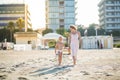 Happy beautiful young mom goes hand in hand with smiling cute child along the sand beach