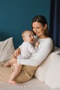 Happy beautiful young mother holds her little son in her arms on the sofa and looks at him with love and a smile Royalty Free Stock Photo