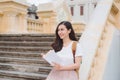 Happy beautiful young woman with backpack and book sitting on stairs outdoors Royalty Free Stock Photo