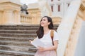 Happy beautiful young woman with backpack and book sitting on stairs outdoors Royalty Free Stock Photo