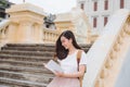 Happy beautiful young woman with backpack and book sitting on stairs outdoors Royalty Free Stock Photo