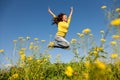 Happy and beautiful young woman in a bright yellow sweater and blue jeans jumping high in a sunny summer field Royalty Free Stock Photo