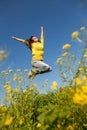Happy and beautiful young woman in a bright yellow sweater and blue jeans jumping high in a sunny summer field Royalty Free Stock Photo