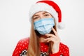 Beautiful young woman in Santa Claus hat and in a medical protective mask on her face, on a white background, Celebrating New Year Royalty Free Stock Photo