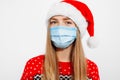 Beautiful young woman in Santa Claus hat and in a medical protective mask on her face, on a white background, Celebrating New Year Royalty Free Stock Photo