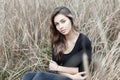 Happy beautiful young woman with a cute smile in a fashionable shirt in stylish jeans is sitting in the dry autumn grass outdoors Royalty Free Stock Photo