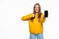 Happy beautiful young woman holding blank screen mobile phone and pointing finger over white background Royalty Free Stock Photo