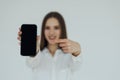 Happy beautiful young woman holding blank screen mobile phone and pointing finger over white background Royalty Free Stock Photo