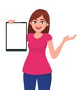 Happy beautiful young woman holding / showing a blank clipboard and showing hand to copy space side away.