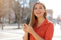 Happy beautiful young woman looking at camera and holding mobile phone outdoor with blurred street on background. City lifestyle Royalty Free Stock Photo