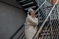 Happy beautiful young woman model with cute smile in a fashionable spring vintage knitted hat in an eco fur coat poses on an iron Royalty Free Stock Photo