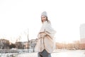 Happy beautiful young woman model with funny smile in a fashionable warm vintage knitted hat in an eco fur coat poses outdoors in Royalty Free Stock Photo