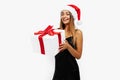 Happy beautiful young woman in a red Santa Claus hat and in a black elegant dress, with a gift on a white background, holiday Royalty Free Stock Photo