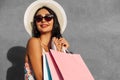 Happy beautiful young woman in summer hat, wears dress and sunglasses holds bags isolated on gray background Royalty Free Stock Photo