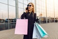 Happy beautiful young woman in sunglasses, with shopping bags, talking on a mobile phone in the background of a shopping center Royalty Free Stock Photo