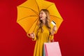 Happy beautiful young woman with umbrella holding shopping bags and credit card on red background, shopping concept, autumn Royalty Free Stock Photo