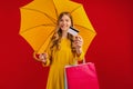 Happy beautiful young woman with umbrella holding shopping bags and credit card on red background, shopping concept, autumn Royalty Free Stock Photo