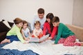 Happy big family is having fun together in bedroom. Large family morning concept. Four kids with parents wear pajamas read book in