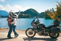 Happy biker couple in love travel together. Stands by a motorcycle with bags. Tourism and vacation. Sunny summer day. Bled lake,