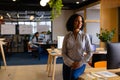 Happy biracial casual businesswoman leaning against desk in office Royalty Free Stock Photo