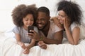 Happy biracial family watch funny video on cell in bedroom Royalty Free Stock Photo