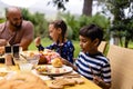 Happy biracial father, son and daughter sitting at table having meal and talking in garden Royalty Free Stock Photo