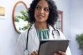 Happy biracial female doctor wearing sthethoscope, using tablet at doctor\'s office Royalty Free Stock Photo