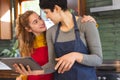 Happy biracial lesbian couple preparing food, using tablet and embracing in kitchen Royalty Free Stock Photo