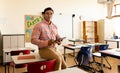 Happy biracial male teacher with tablet in elementary school classroom Royalty Free Stock Photo