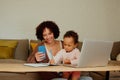 Happy biracial mother and daughter using mobile phone near laptop in living room at home Royalty Free Stock Photo