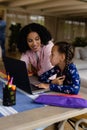 Happy biracial mother helping daughter using laptop for schoolwork talking at home, copy space Royalty Free Stock Photo