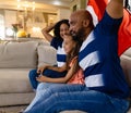 Happy biracial parents and daughter sitting on couch watching tv holding french flag and cheering