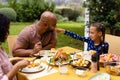 Happy biracial parents and daughter at table having meal and tasting each other's food in garden Royalty Free Stock Photo