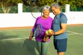 Happy biracial senior couple with tennis balls, rackets and water bottle standing in tennis court Royalty Free Stock Photo