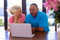 Happy biracial senior man and caucasian woman watching video over laptop while sitting at table Royalty Free Stock Photo