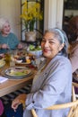 Happy biracial senior woman celebrating with friends at christmas dinner in sunny dining room Royalty Free Stock Photo