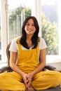 Happy biracial teenage girl having video call sitting cross legged in sunny room smiling Royalty Free Stock Photo