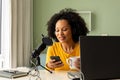 Happy biracial woman using headphones, laptop and microphone podcasting from home Royalty Free Stock Photo