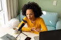 Happy biracial woman using headphones, laptop and microphone podcasting from home Royalty Free Stock Photo