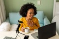 Happy biracial woman using headphones, laptop and microphone podcasting from home Royalty Free Stock Photo