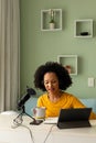 Happy biracial woman using headphones, tablet and microphone podcasting from home Royalty Free Stock Photo