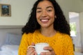 Happy biracial woman in yellow sweater holding cup of coffee at home Royalty Free Stock Photo